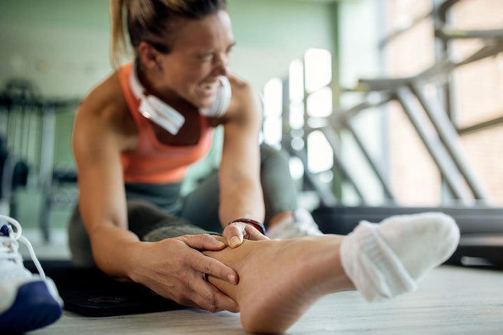 Bild på kvinna som tar sig om fotleden och grimaserar på grund av smärta i fotleden