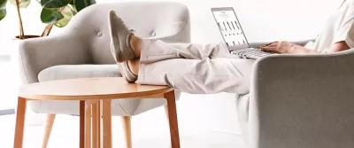 4 tips til at modvirke hævede ben Person sidder med computer på skødet i sofaen med fødderne på bordet
